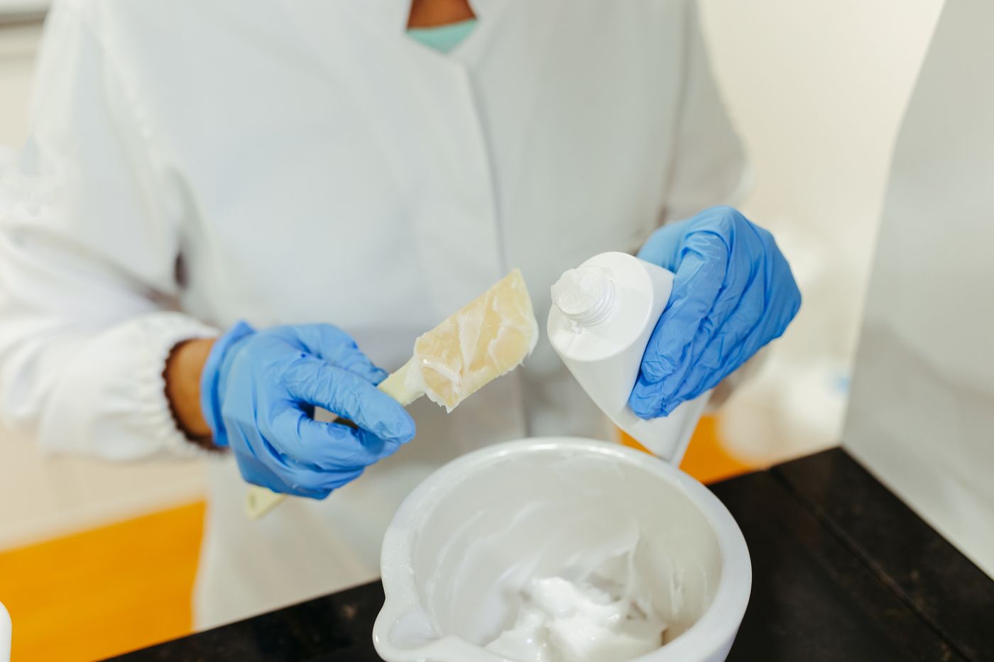 Gloved hands blending a cosmetic cream sample during formulation development in a lab